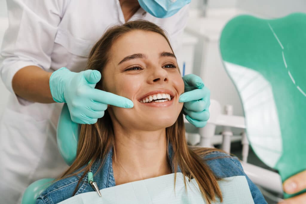 Patient smiling into a hand mirror in the dental chair during a veneer consultation in Beachwood, OH